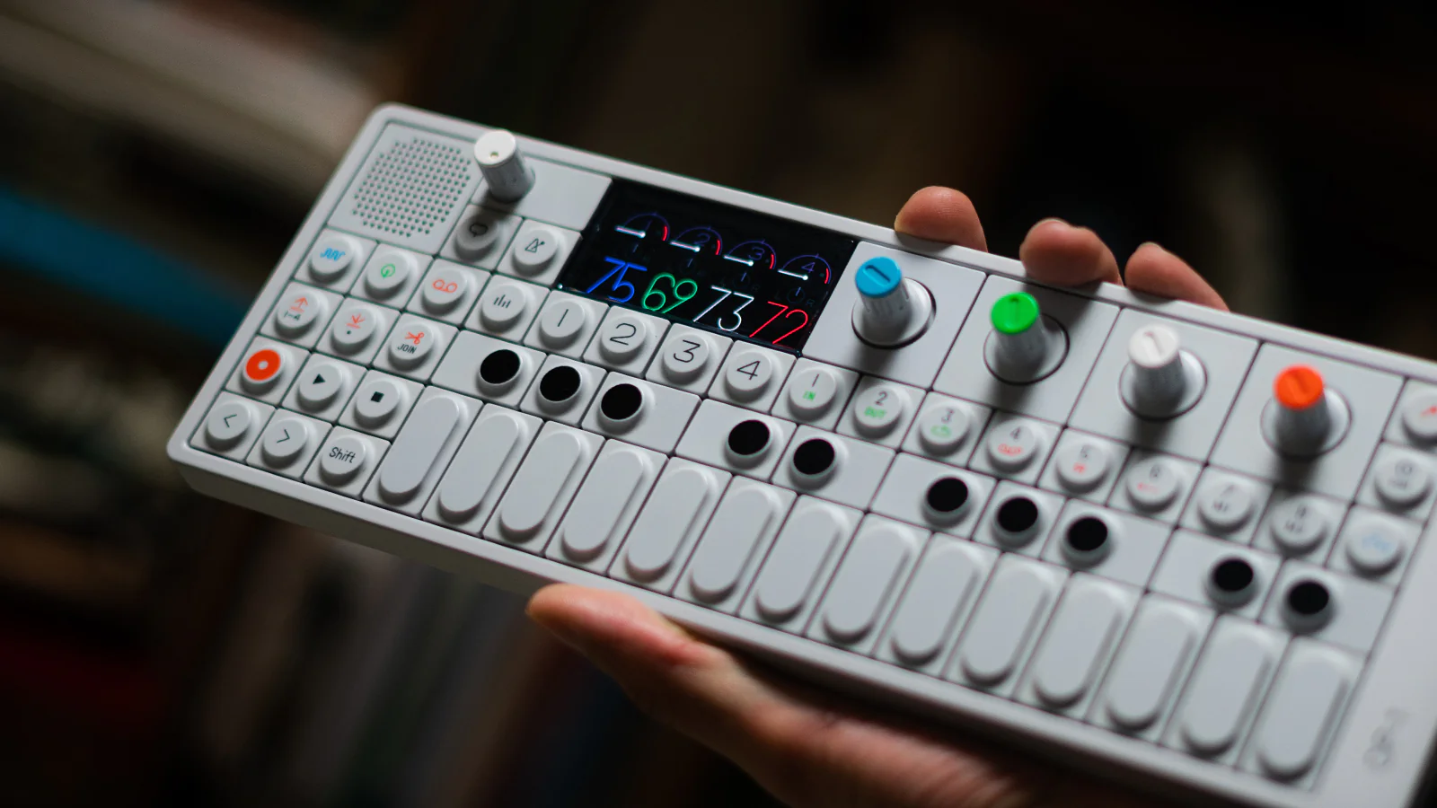 Compact music production workstation with an external effects module and coiled cable, arranged over graphic prints and technical documentation.
