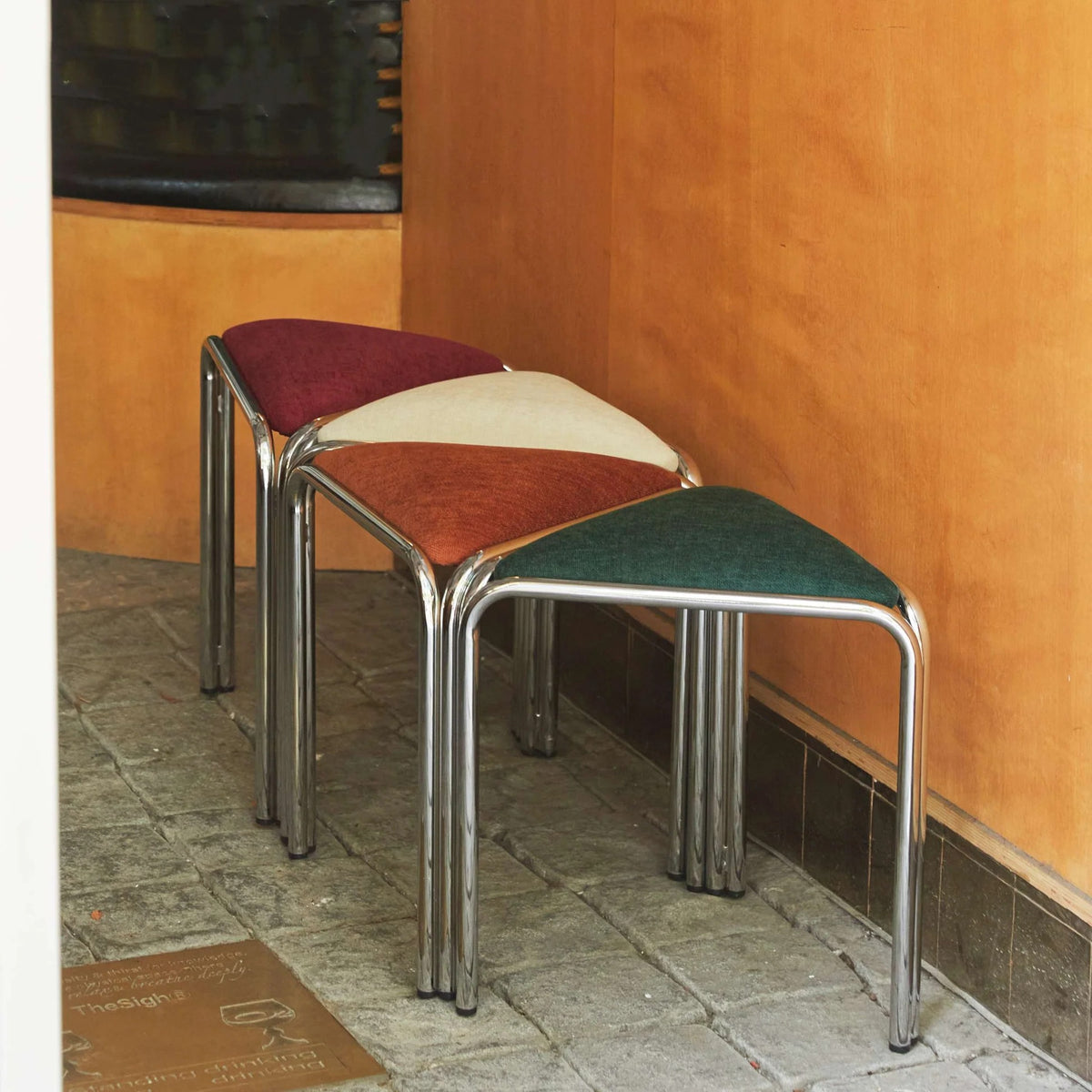 Four triangle stacking stools in burgundy, white, orange, and green nested together